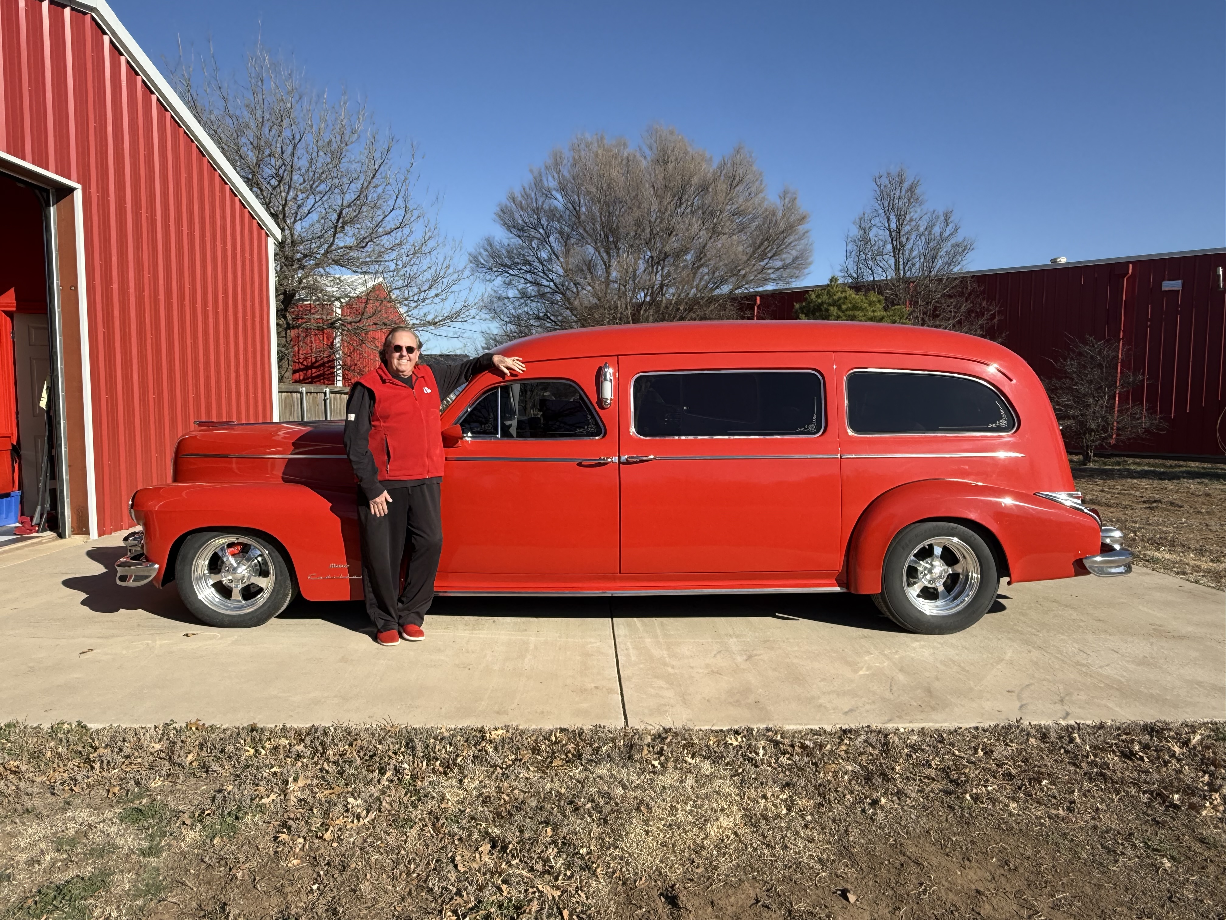 Billy Krause standing beside his red 1948 Cadillac hearse