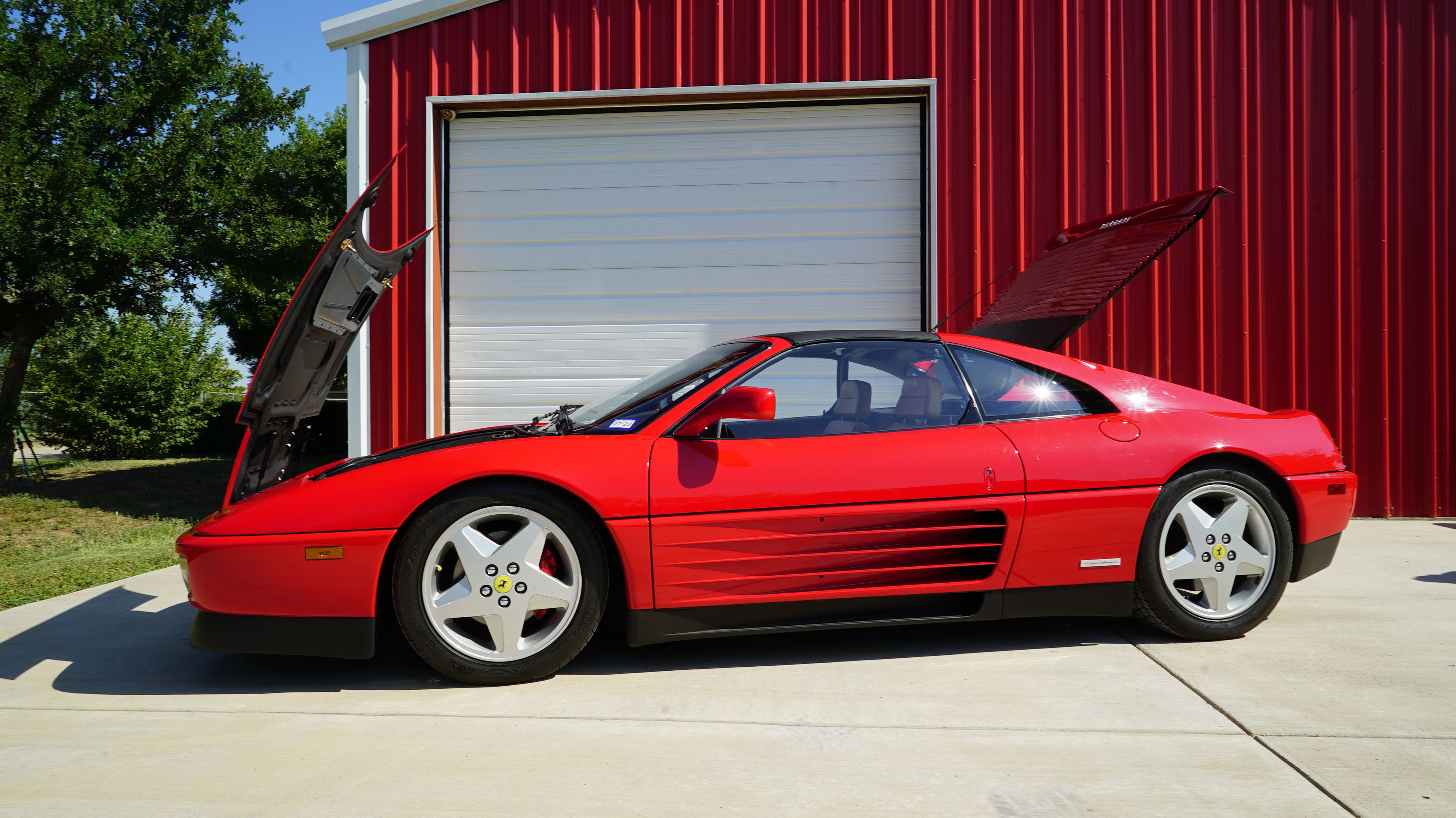 Red Ferrari 348 with its front and rear panels open outside the garage
